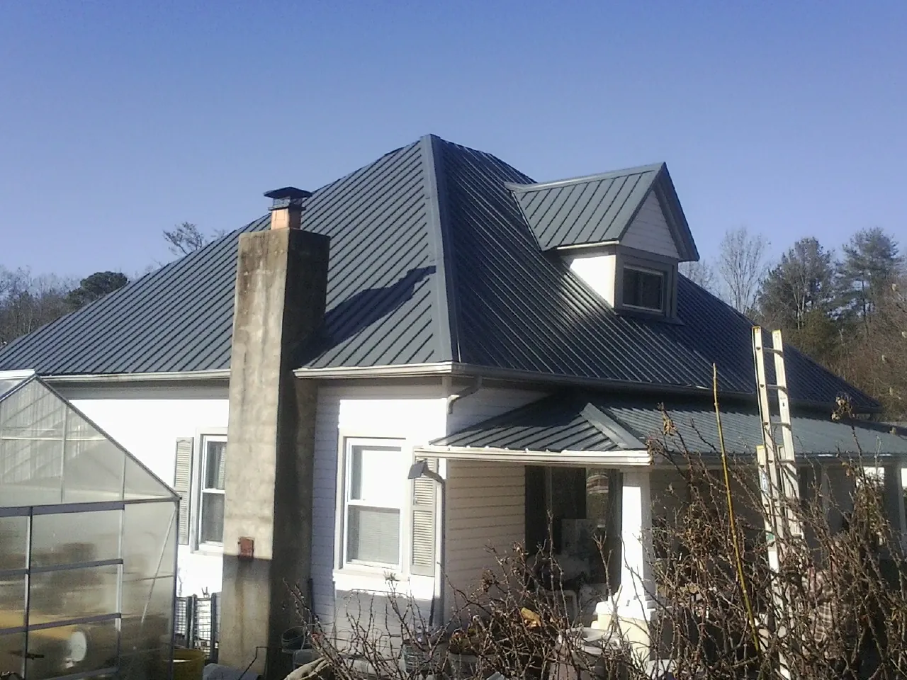 Dark blue standing seam metal roof on a white farmhouse with dormer — Slate & Tile Roof Repair by Roofing Brothers in Highland