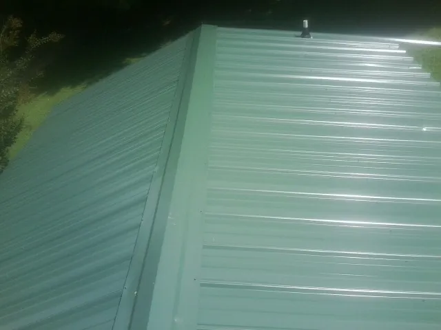 New green metal panels meeting at the ridge of a roof — Flat Roof Repair work by our crew in Highland
