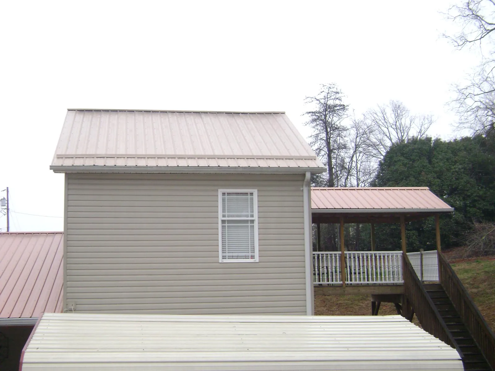 Tan metal roofs on a two story addition and attached porch, from a Roof Replacement job in Highland